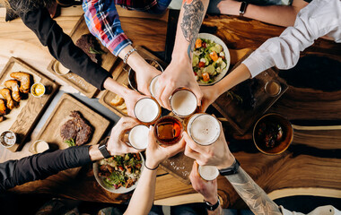 Friends cheering beer glasses on wooden table covered with delicious food - Top view of people having dinner party at bar restaurant - Food and beverage lifestyle concept - 603121441