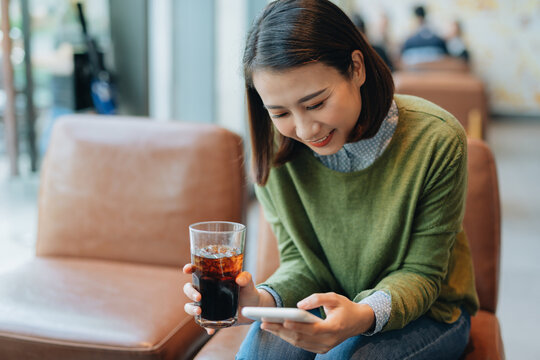 Asian woman holding coffee cup and play smart phone in coffee shop