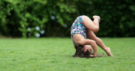 Happy child girl rolling on lawn outdoors, tumbling down, kid doing somersault