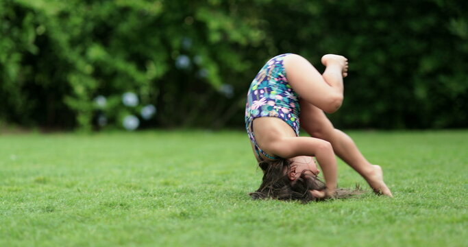Happy child girl rolling on lawn outdoors, tumbling down, kid doing somersault