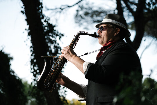 Male musician in sunglasses playing saxophone in park