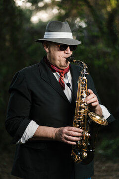 Adult man in hat playing saxophone at park