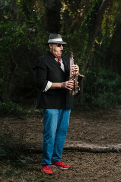 Adult man playing saxophone in forest during weekend