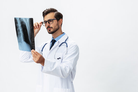 Male doctor in white coat and eyeglasses and stethoscope looks thoughtfully at pictures of X-ray patient for diagnosis on white isolated background, copy space, space for text, health