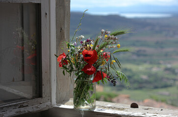 Bouquet of wild flowers with poppies and other flowers on the windowsill against the backdrop of tuscany