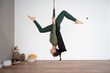 Flexible woman performing aerial yoga pose in studio