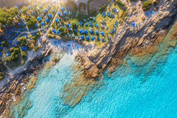 Fototapeta na wymiar Aerial view of sea bay, sandy beach with umbrellas, stones and rocks in water at sunset in summer. Sardinia, Italy. Tropical scenery with sea lagoon, swimming people, blue water. Drone view from above