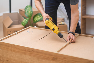 Furniture installation specialist in uniform assembling a wooden rack, attaching legs with an...