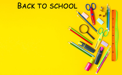 On a yellow background, a flat lay of stationery items for school, colored pencils, a magnifying glass, felt-tip pens, a calculator, scissors.  Back to school concept.  Space for copy text.