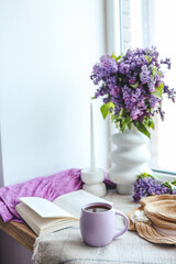 Cup of tea, straw hat, open book and lilac basket, spring still life
