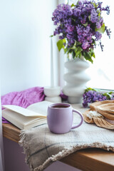 Cup of tea, straw hat, open book and lilac basket, spring still life