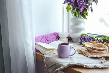 Cup of tea, straw hat, open book and lilac basket, spring still life