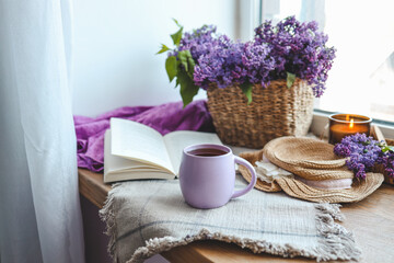 Cup of tea, straw hat, open book and lilac basket, spring still life