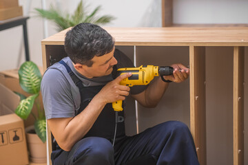 Custom furniture production and installation firm employee using drilling machine making holes in...