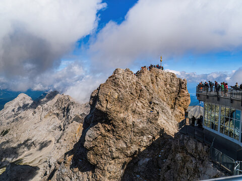 Tourists and mountain climbers on the Zugspitze mountain top summit cross and lookout platform, cable car station during summer