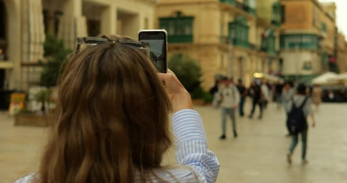 Tourist female student press shutter button in camera app on phone in street. View of smartphone screen while unrecognizable young woman takes photo in old downtown.