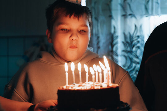 Overjoyed smiling boy with party cone blowing out candles at birthday 