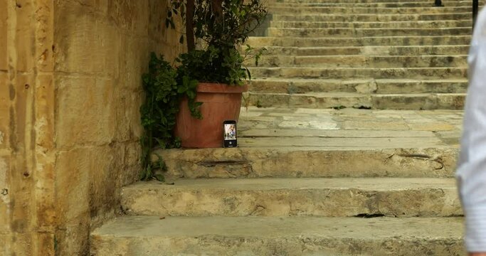 Young woman start countdown in camera app on phone stand on ancient stairs. Female tourist use self timer on smartphone to automatically take photo remotely in antique city.
