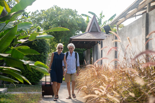 Senior Couple Walking With Suitcase In Resort Area