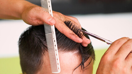 barber cutting a young man's hair with scissors and a comb