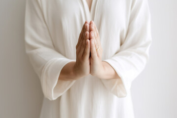 A pair of hands, folded in prayer, against a clean and serene background