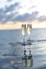 Two glasses of champagne on the side of the infinity pool against the backdrop of a sunset in the Maldives