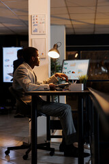 Fototapeta na wymiar Businessman looking at computer screen analyzing financial graphs report, working late at night at company strategy. African american executive manager planning investment plan
