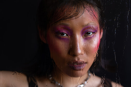 Asian woman with fashion pink makeup through wet glass 