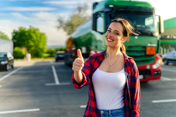 Junior female truck driver standing in front of her truck after she successfully completed her first tour thumps up for a job well done