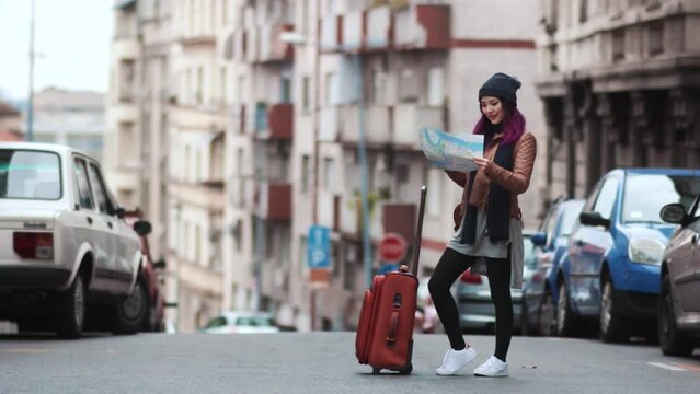 City girl tourist with a luggage studying a map. A cute Asian girl spends the summer on vacation in Europe. The girl is happy and enjoys life. A woman walks through the European streets. Friendship