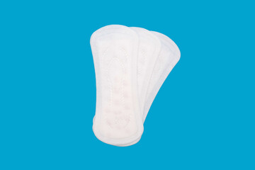 Three feminine hygiene menstrual pads arranged in a fan shape on a blue background. Feminine hygiene product in the form of sanitary pads. Clean menstrual pads ready to use