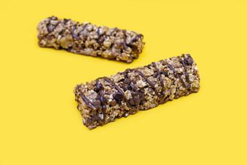 Two bars of oatmeal and chocolate on a yellow background. Delicious healthy snack and energy in the form of carbohydrates. Healthy food in the form of a bar of oatmeal and healthy cereals