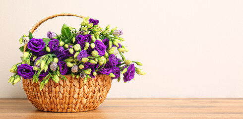 Obraz na płótnie Canvas Basket with beautiful eustoma flowers on table near light wall. Banner for design