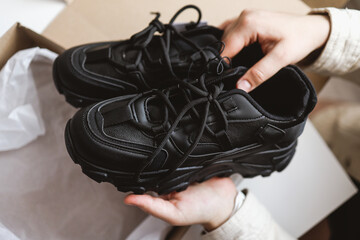 Unpacking women's shoes, stylish black sneakers in hands