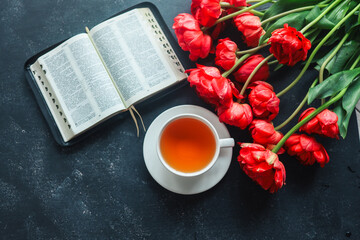 Open bible with tulip flowers and a cup of tea on a dark background