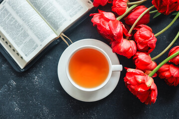 Open bible with tulip flowers and a cup of tea on a dark background