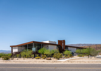 Obraz premium Borrego Springs, CA, USA - April 24, 2023: full frontal view on modern architecture style public Library building under blue sky, set on sandy desert floor with green bushes. US flag present