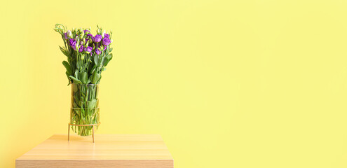 Vase with beautiful eustoma flowers on table near yellow wall. Banner for design
