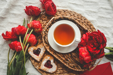 Tray with tasty breakfast, bouquet of peonies and gift for Valentine's Day on bed