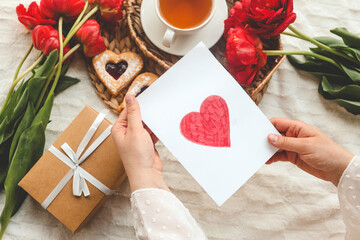 Woman hands holding a beautiful hand drawn Mother's Day greeting card with red envelope, I Love You Mom message on the card