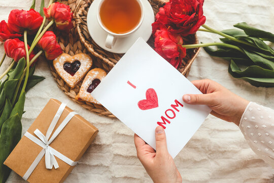 Woman hands holding a beautiful hand drawn Mother's Day greeting card with red envelope, I Love You Mom message on the card