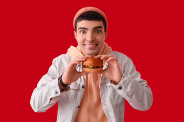 Young man with tasty burger on red background