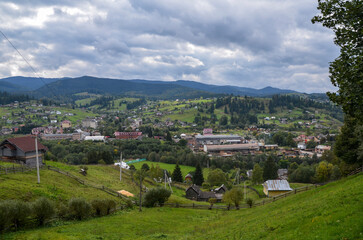 Picturesque scenery of rolling countryside with rural houses of a Carpathian mountain village on green hills under cloudy sky. Vorokhta, Ukraine