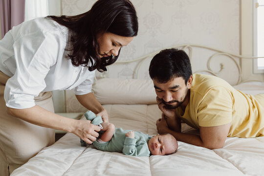 Mother changing clothes of baby near father on bed