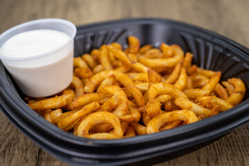 To go order of crispy curly fries packed in plastic container with dressing on the side