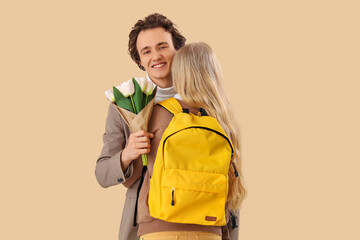 Teenage girl hugging her boyfriend with tulips on beige background