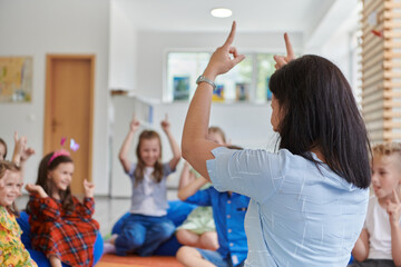 A happy female teacher sitting and playing hand games with a group of little schoolchildren