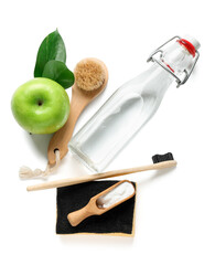 Bottle of vinegar, baking soda, brushes, sponge and apple on white background