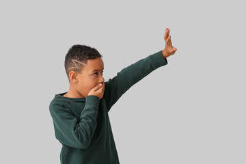 Scared little African-American boy on light background