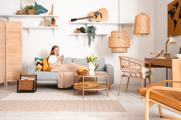 Beautiful young woman using mobile phone on sofa in stylish living room